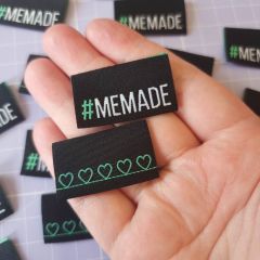 A hand holding a black woven sew-in label featuring the word #MEMADE 