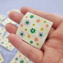 A hand holding a cream, square-shaped sew-in label covered in pretty multi-coloured flowers