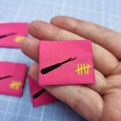 A hand holding out a hot pink woven sew-in label with a black seam ripper